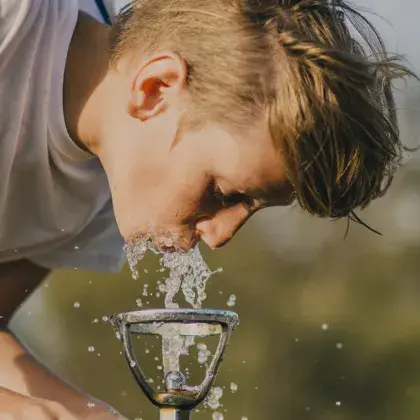 Man sieht einen Jungen, der Wasser aus einem öffentlichen Wasserhahn trinkt.